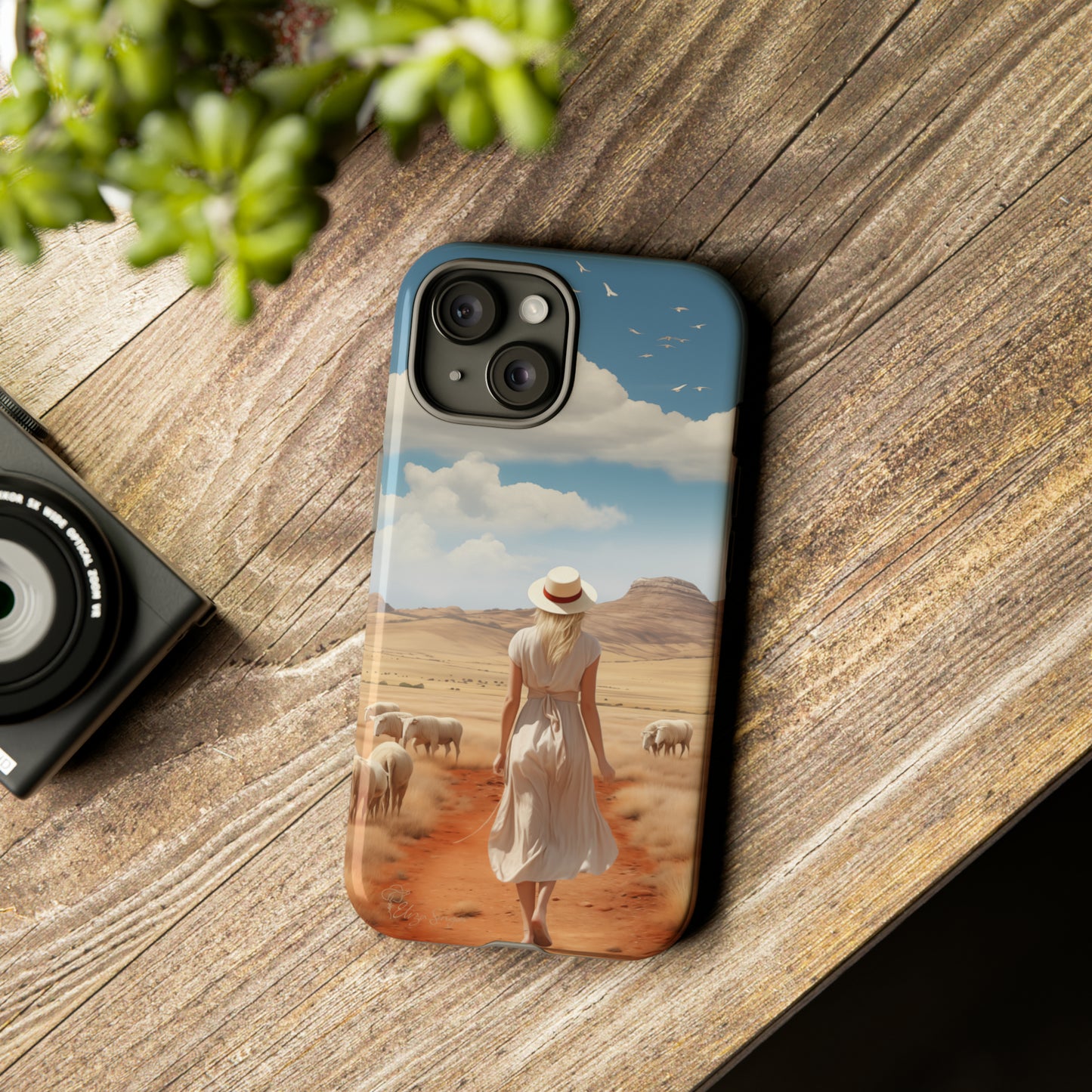 Serenity in Hand: Our Tough Western Cell Phone Case invites you to experience tranquility. A vintage painted design portrays a woman in a skirt and hat walking on a dirt road through a prairie, with grazing sheep. Let the vanishing horizon captivate your senses. Elevate your phone with timeless beauty. #ElizaSinger #PhoneCase