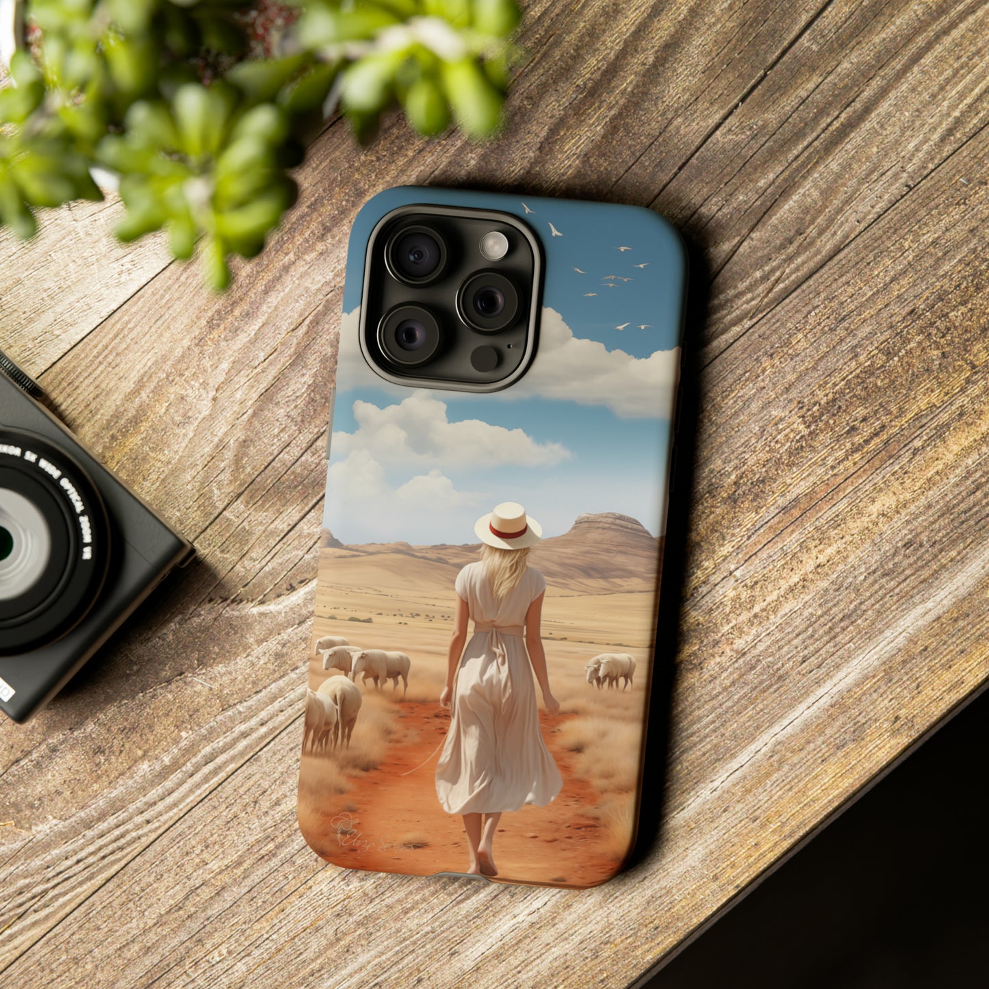 Serenity in Hand: Our Tough Western Cell Phone Case invites you to experience tranquility. A vintage painted design portrays a woman in a skirt and hat walking on a dirt road through a prairie, with grazing sheep. Let the vanishing horizon captivate your senses. Elevate your phone with timeless beauty. #ElizaSinger #PhoneCase