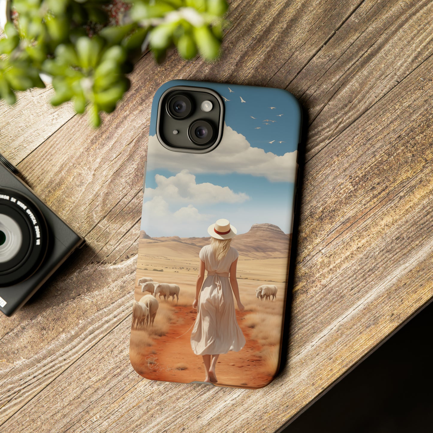 Serenity in Hand: Our Tough Western Cell Phone Case invites you to experience tranquility. A vintage painted design portrays a woman in a skirt and hat walking on a dirt road through a prairie, with grazing sheep. Let the vanishing horizon captivate your senses. Elevate your phone with timeless beauty. #ElizaSinger #PhoneCase