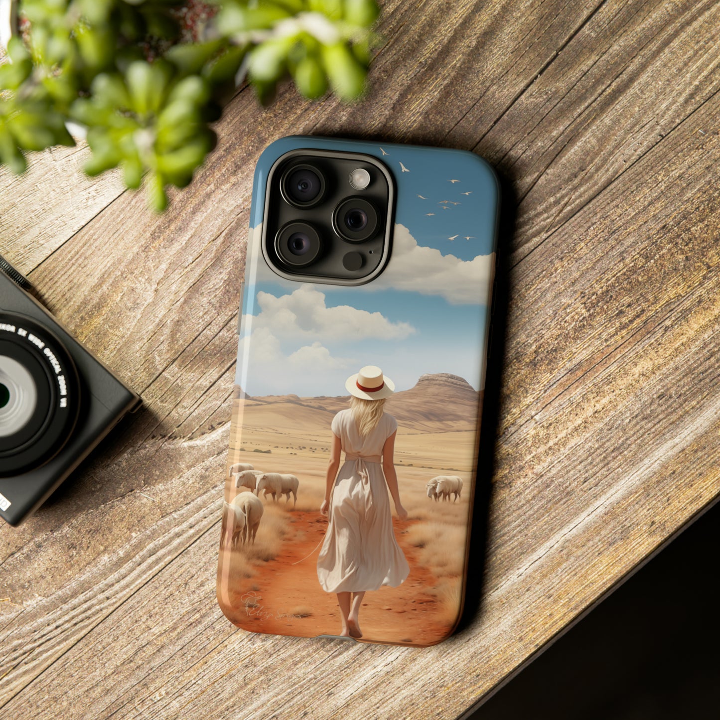 Serenity in Hand: Our Tough Western Cell Phone Case invites you to experience tranquility. A vintage painted design portrays a woman in a skirt and hat walking on a dirt road through a prairie, with grazing sheep. Let the vanishing horizon captivate your senses. Elevate your phone with timeless beauty. #ElizaSinger #PhoneCase