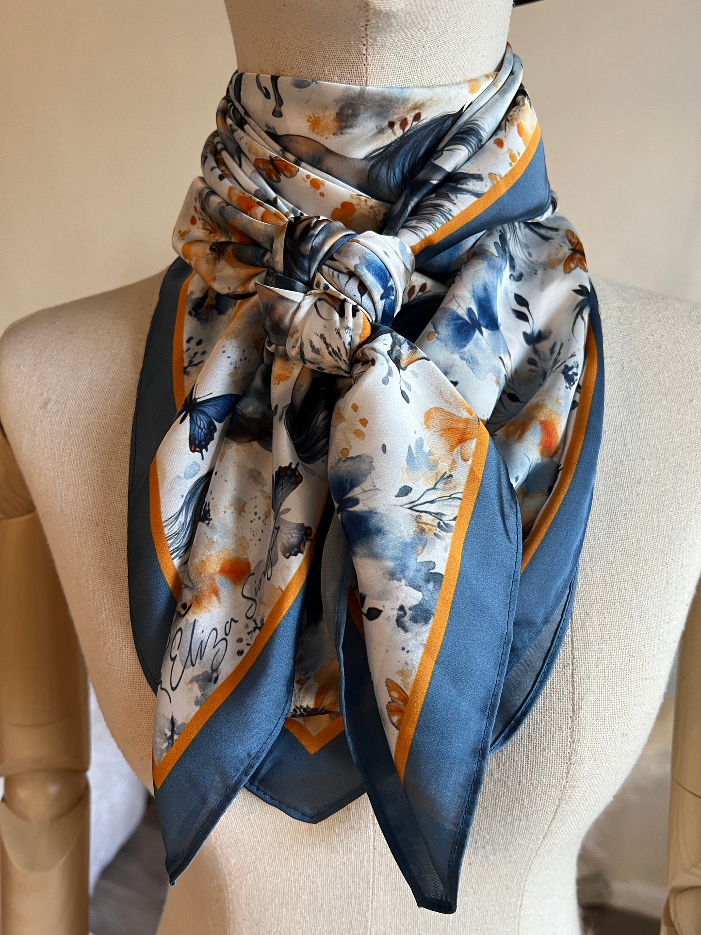 Wings & Whinnies — a dreamy satin silk wild rag featuring galloping horses and butterflies. Designed on the diagonal and signed by Eliza Singer.