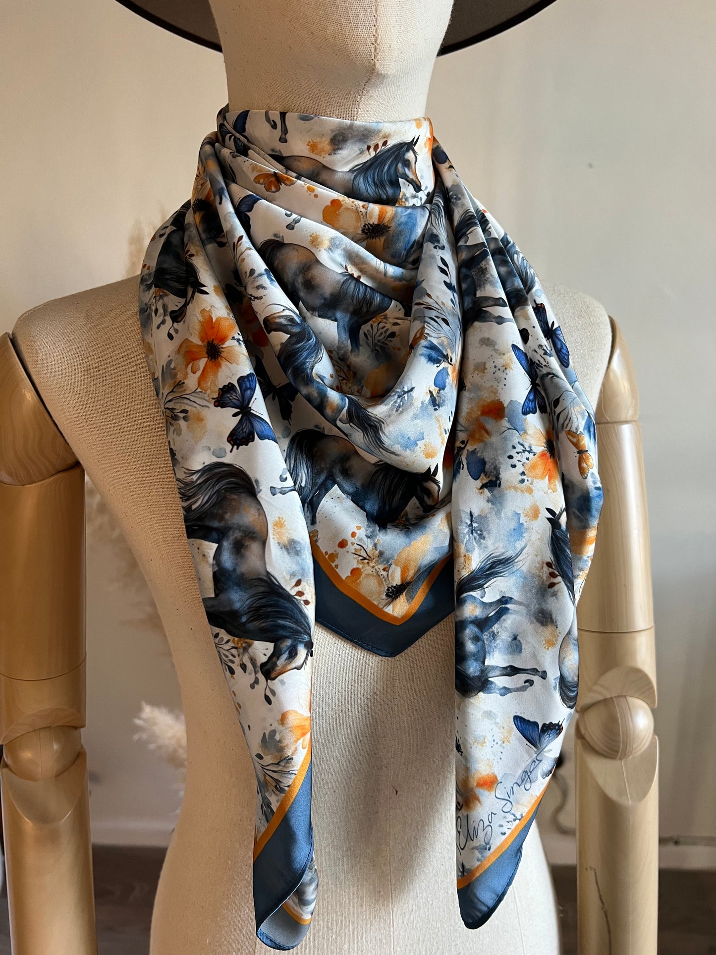 Wings & Whinnies — a dreamy satin silk wild rag featuring galloping horses and butterflies. Designed on the diagonal and signed by Eliza Singer.