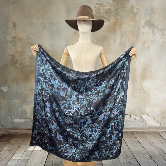 Embrace mystery with our Moody Garden Shadows Wild Rag. Against a black background, muted botanical prints create a captivating 39" square of

100% satin silk. Elevate your wardrobe with this unique and enigmatic accessory.